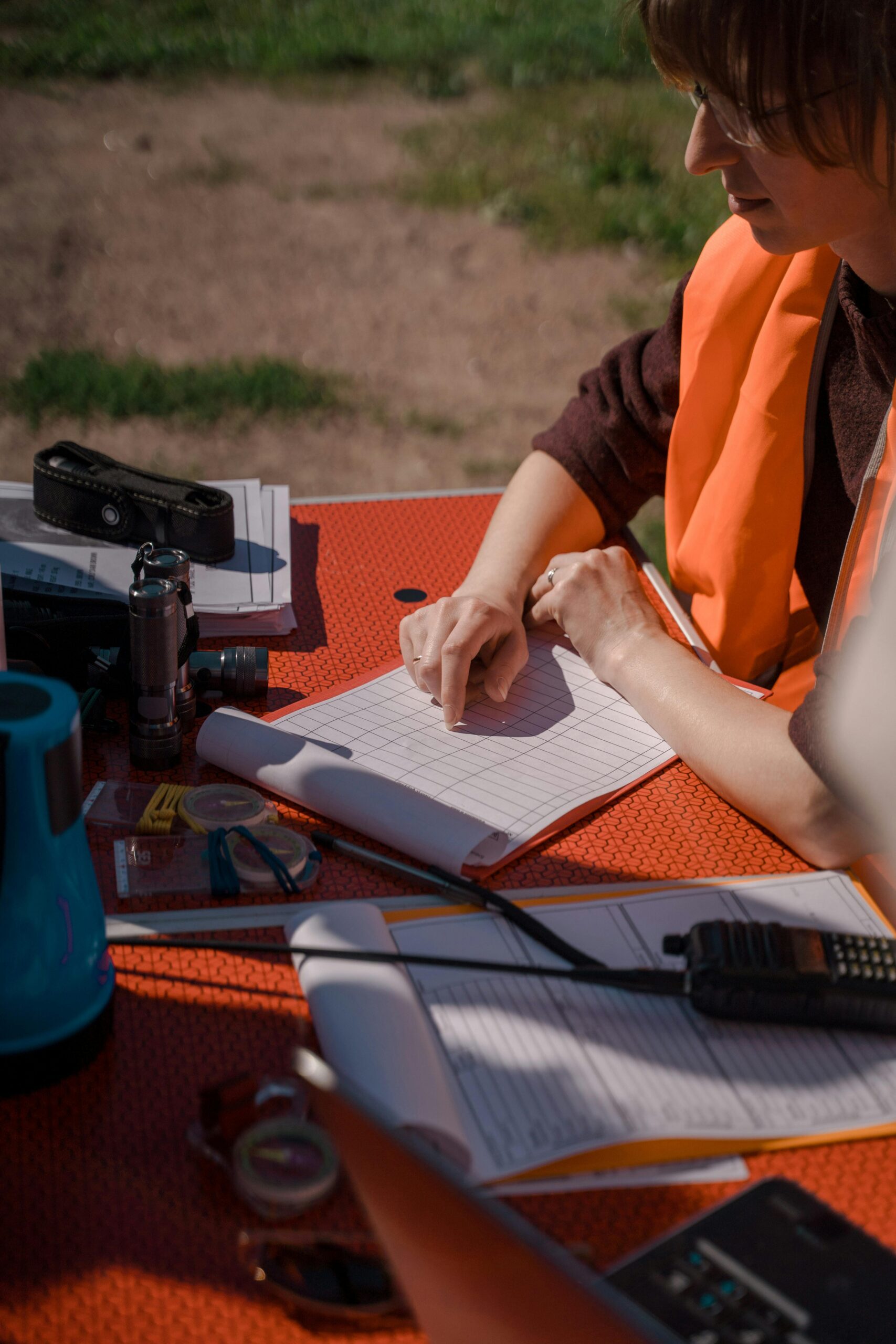 Individual in a safety vest working outdoors with notes and radio equipment.