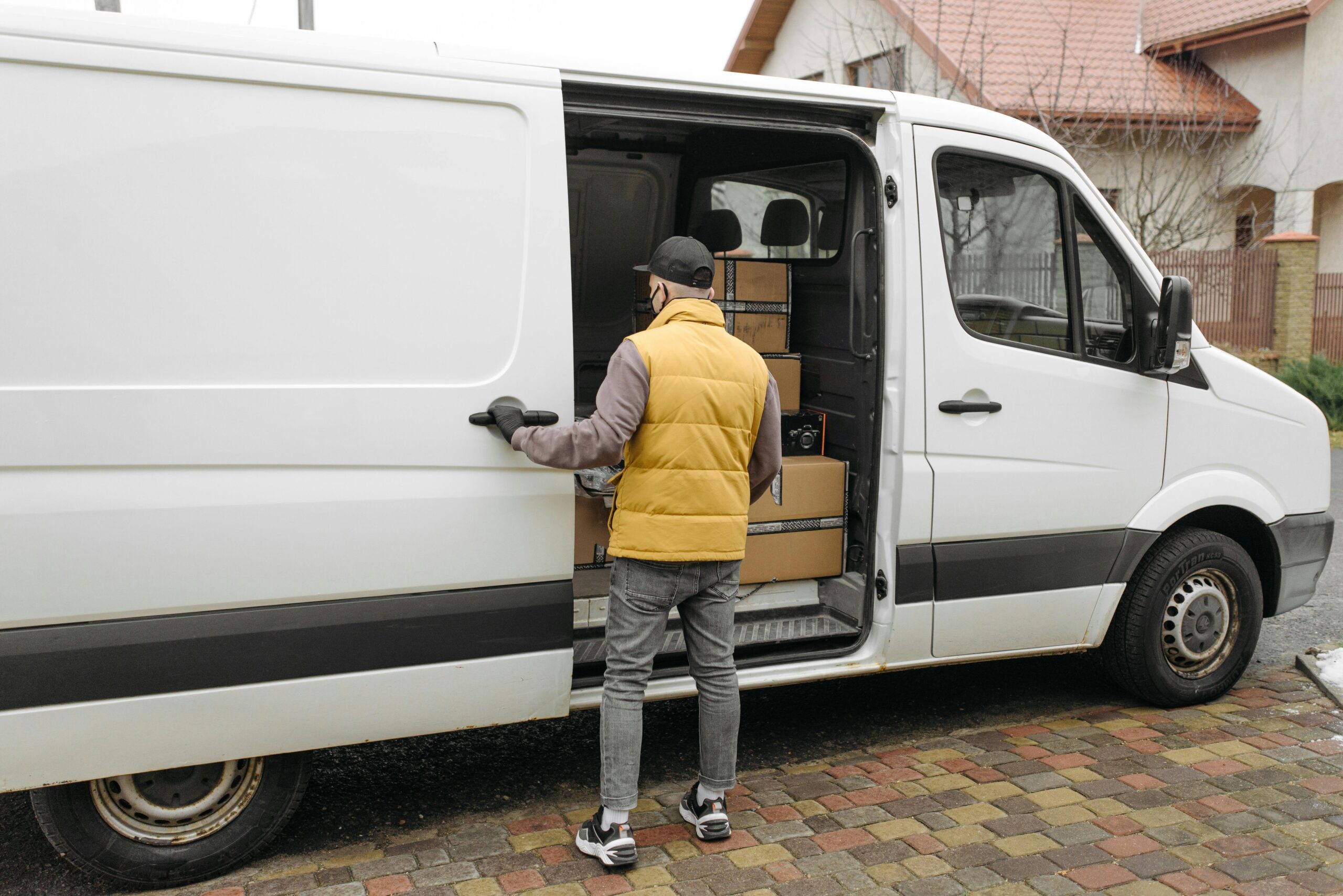 A delivery driver loads packages into a white van on a residential street.